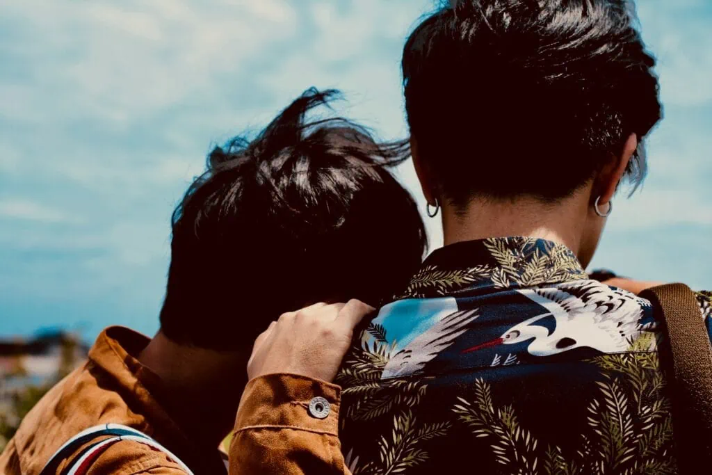Two queer LGBTQIA+ butch people with short dark hair, one is resting their head on the other's shoulder.