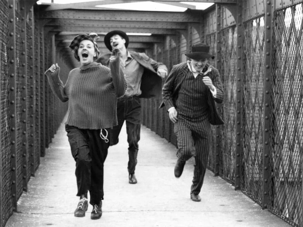 A black and white still of three polyamorous lovers running across a bridge from the 1962 French New Wave film ‘Jules et Jim.’