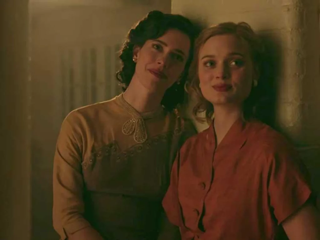A still from ‘Professor Martson and Wonder Woman’ with Rebecca Hall and Bella Heathcote. They are both leaning against a wall together, their shoulders touching. 