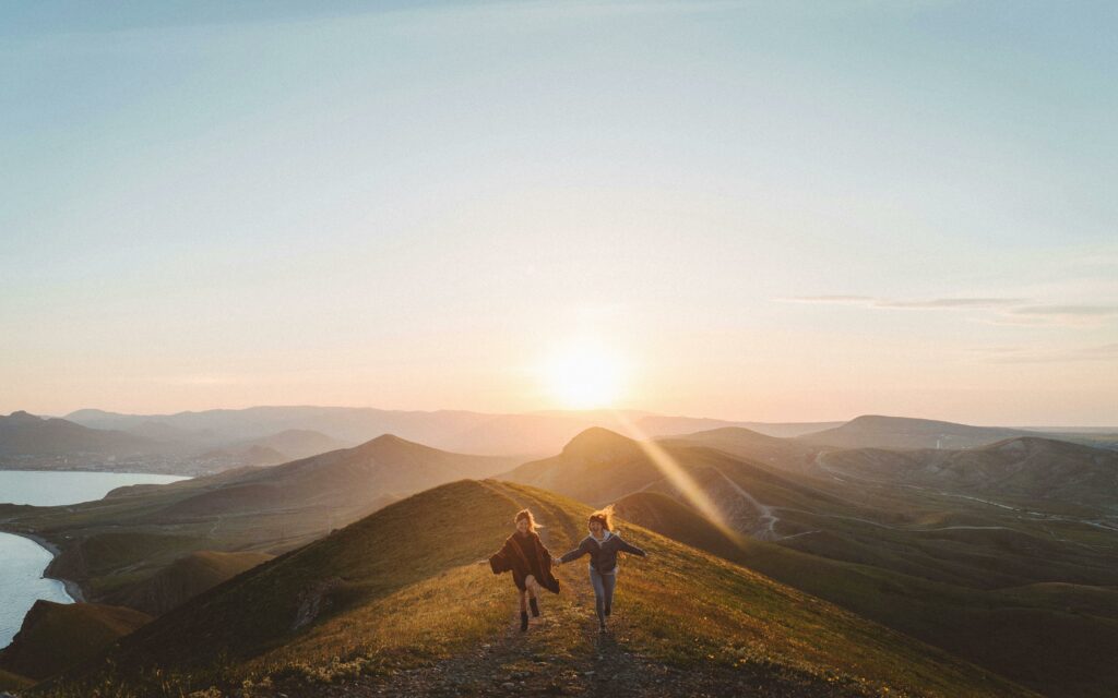 Lesbian couple running on a mountain at sunset 