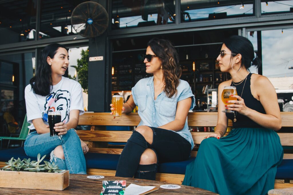 Three women chat on a bench at a local queer bar, a good option for finding other queer women.