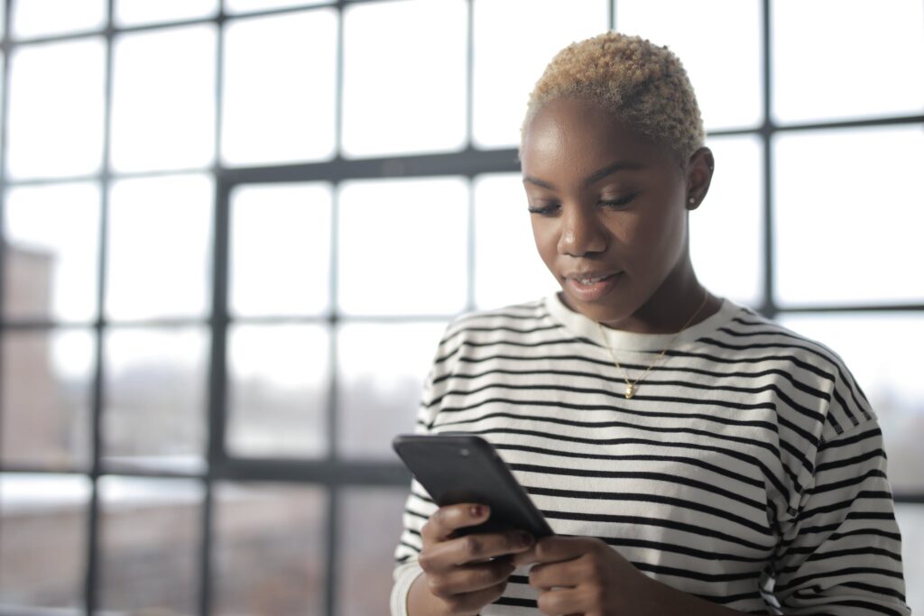 A non-binary lesbian smiles as they read something on their phone, probably an online chat with another queer woman.