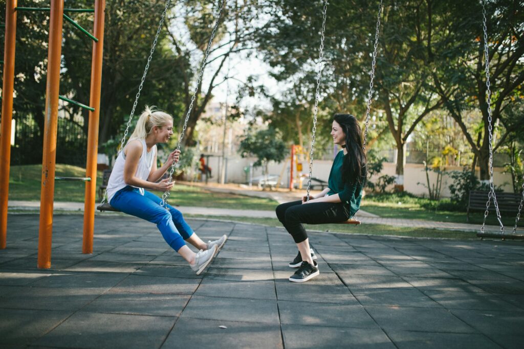 Two women sit opposite each other on swings at a park. They may be discussing their dating or relationship goals.