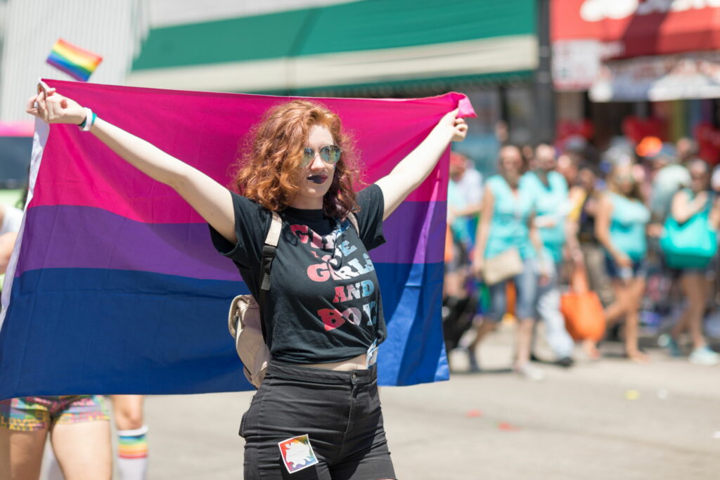 Woman at pride lifting a bisexual flag.