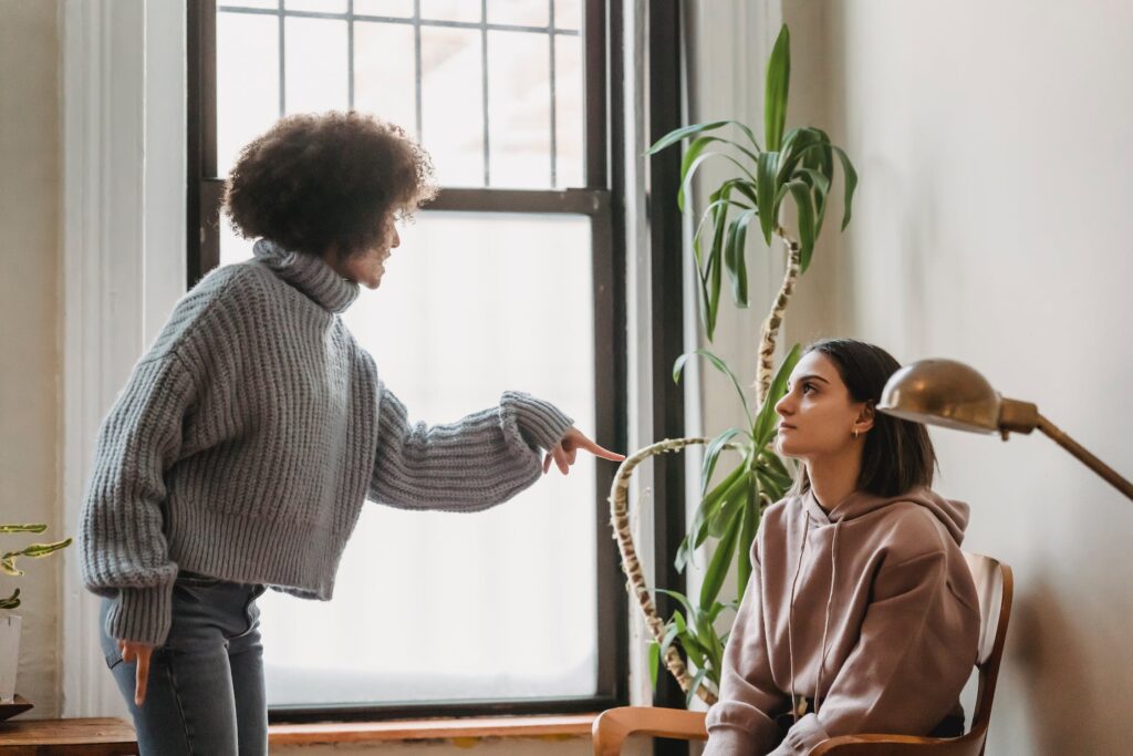 A lesbian couple struggle to establish communication skills and relationship needs. One points the finger at the other person sitting, as if they’re disagreeing.