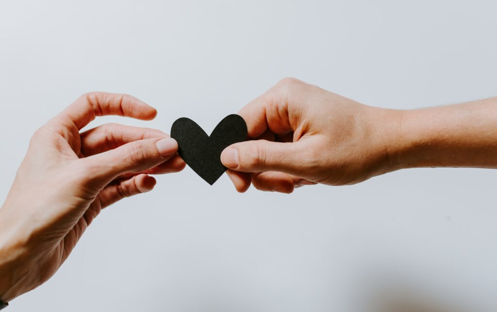 Two hands reach out for a paper cutout of a heart, symbolizing building trust in relationships, reaching out to your partner, and exercising effective communication skills.