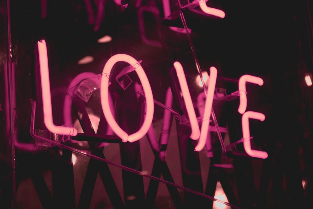 A pink neon sign reading “LOVE” glowing in all capital letters. Deep trust and unconditional love is one of the final stages of a relationship.