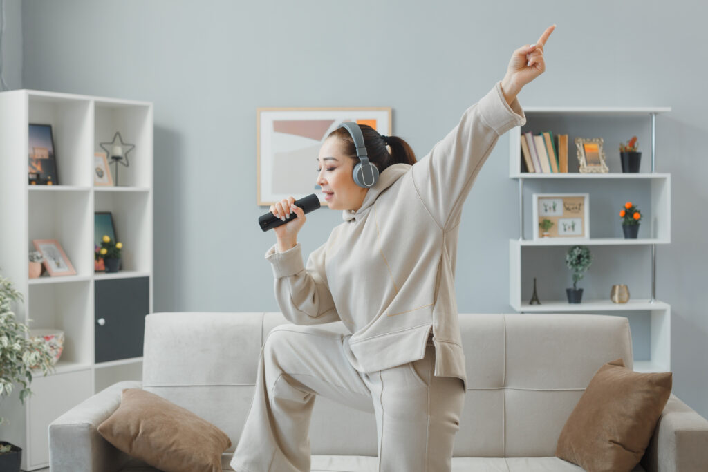 Woman in casual clothing with headphones dancing on a couch at home.