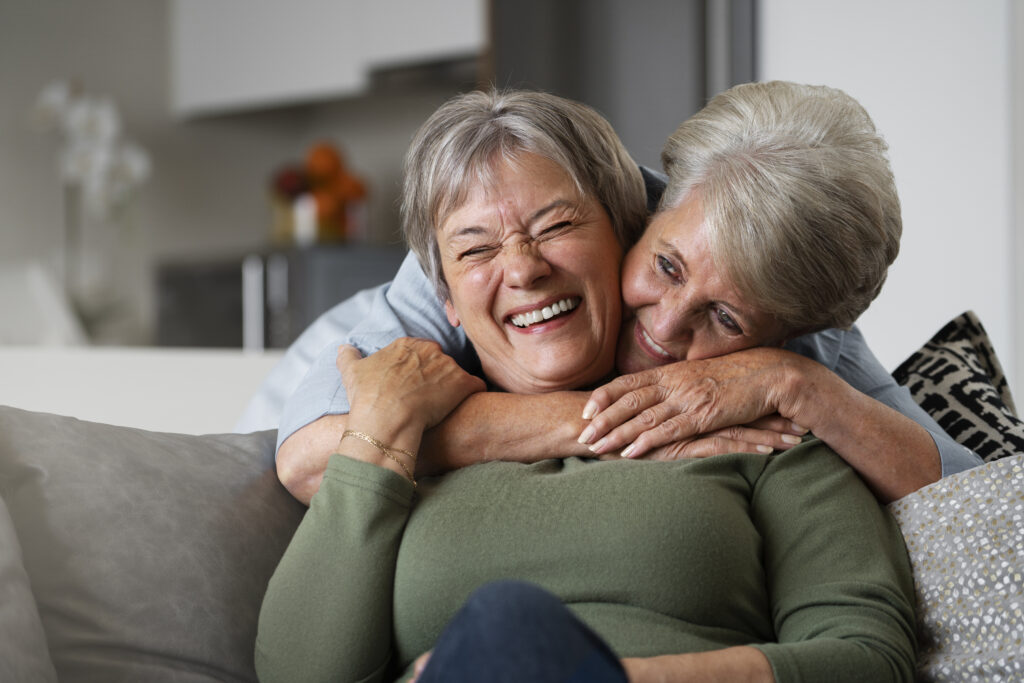Elder sapphic couple hugging lovingly.