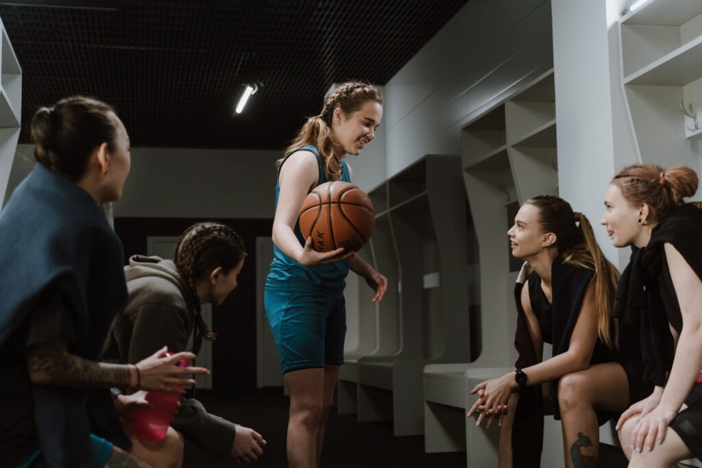 A diverse group of LGBT women in a welcoming and inclusive changing room at an LGBT gym and wellness space in New York, chatting and preparing for their workout sessions.