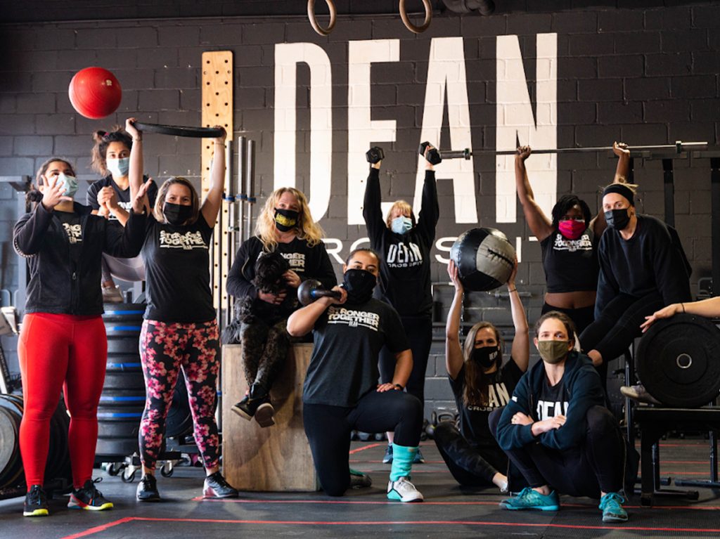 Group of diverse individuals standing and smiling together at Dean CrossFit, an LGBT-friendly gym and wellness space in New York.
