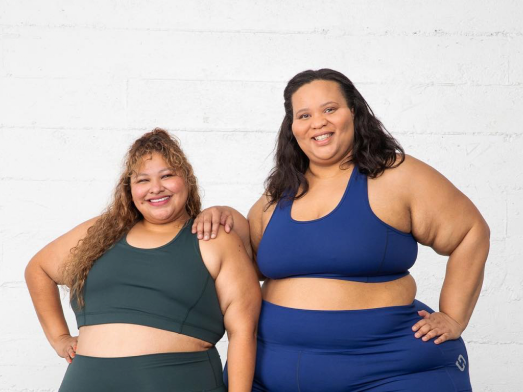A pair of cheerful LGBT women in workout clothes, enjoying their time at Halfpence Moon Yoga, a welcoming gym and wellness center for the LGBT community in New York.