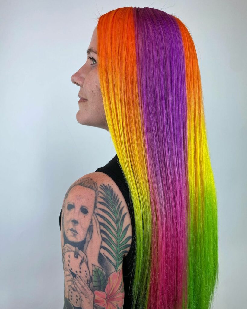 a woman at Fruits Hair Lab, standing with her vibrant rainbow-colored hair being styled, showcasing a spectrum of vivid hues in her hair.