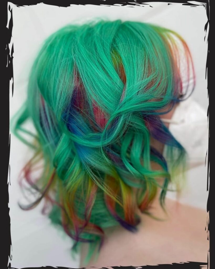 A woman at Studio Strange, standing as she gets her hair styled with vibrant rainbow colors, showcasing a bold and colorful hair transformation.
