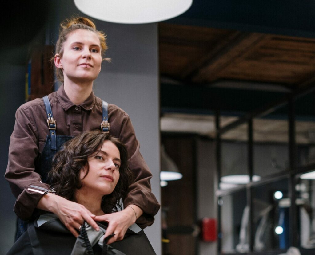 A lesbian woman smiling as she gets her hair styled in a queer-friendly salon, emphasizing a safe and inclusive atmosphere.