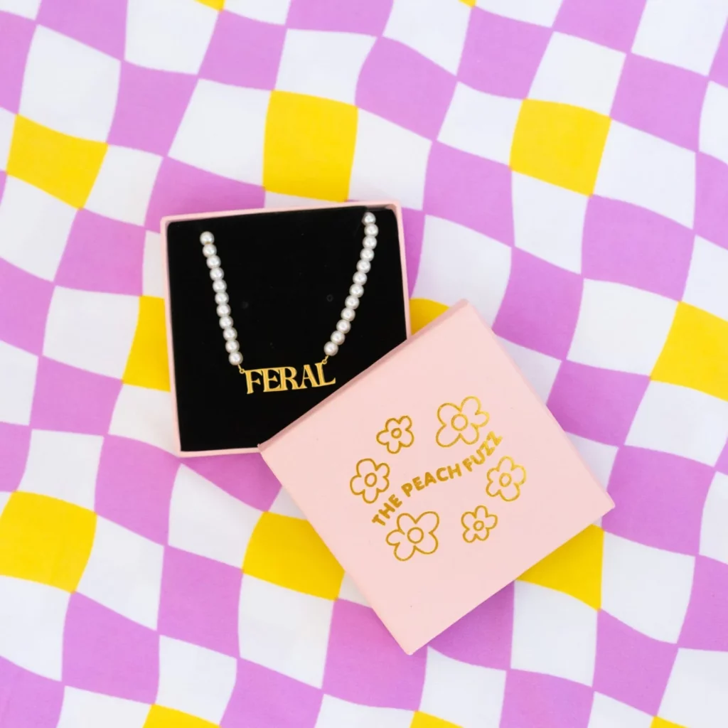 Necklace that says “FERAL” on top of lavender checkered pattern.