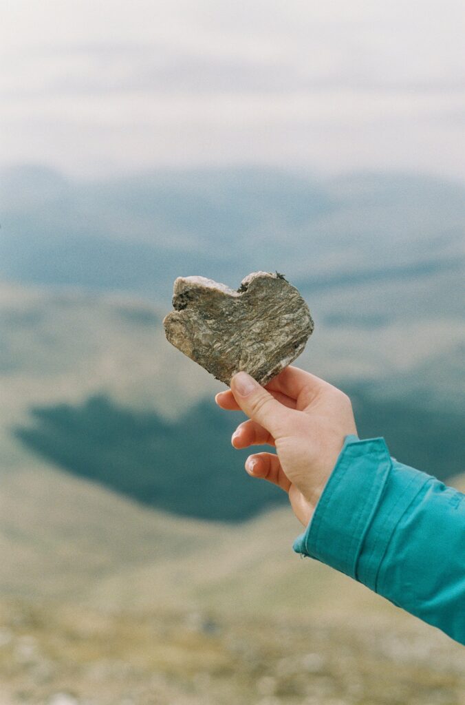 Woman holds a stone heart over a mountain lake 