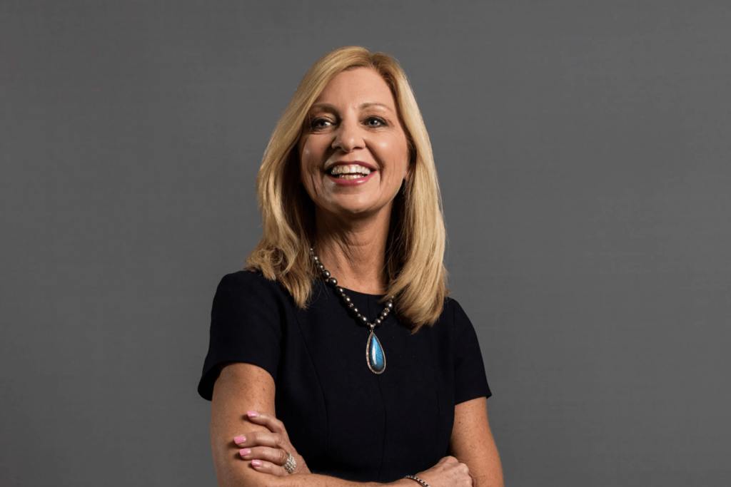 Karen Lynch posing with a smile and arms crossed on a gray background.