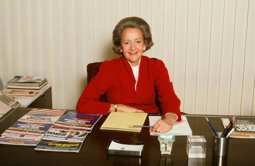 Katherine Graham sitting and smiling on her desk.