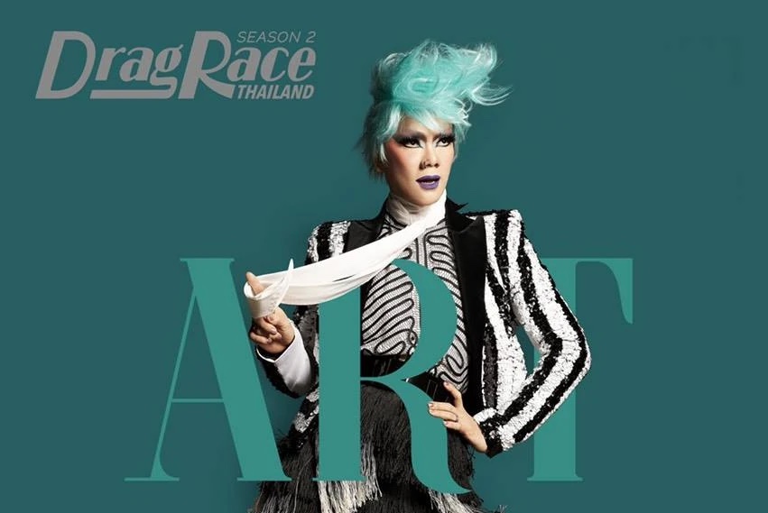 Art Arya from Drag Race Thailand Season 2, striking a fierce pose in a black and white costume with a vivid green wig. One hand is confidently placed on the hip, while the other points to the side, exuding charisma and boldness.