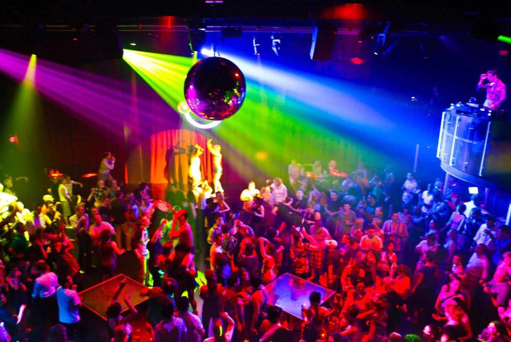 Crowded dance floor inside DJ Station, Bangkok, illuminated by colorful spotlights and neon, showcasing the energetic and inclusive atmosphere of the city's LGBTQIA+ nightlife.