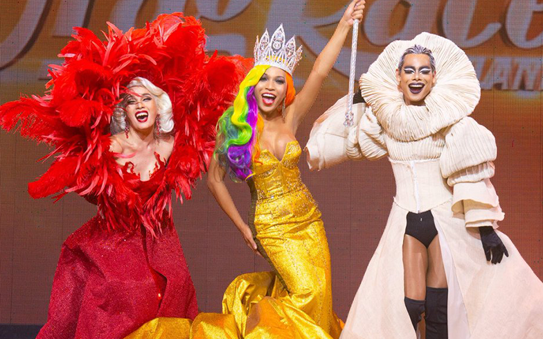Drag queens in glamorous outfits share a triumphant moment on the Drag Race Thailand stage, beaming with happiness.