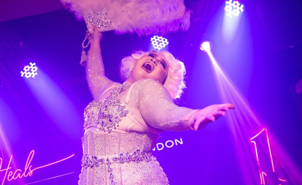 Drag queen passionately performing on stage at House of Heals, adorned with a voluminous blonde wig, dramatically lip-syncing to captivate the audience.