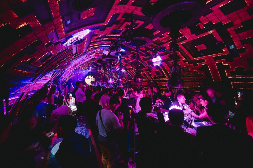 Interior of Lost & Found Bangkok, featuring a lively crowd under a radiant pink spotlight. The venue resembles a stylish cave with a creative and artistic design, exuding a vibrant and enchanting atmosphere.