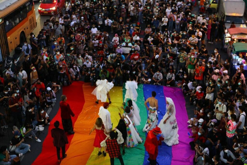 Image showing LGBTQIA+ community and HER joining the Rainbow Party Coalition at Bangkok's Pride event, proudly walking together on a large rainbow flag.
