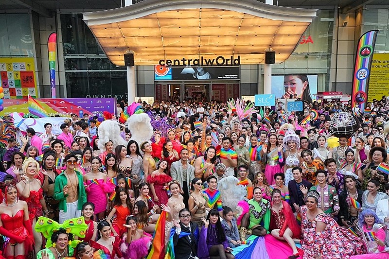 An energetic and colorful scene at the Rainbow Runway for Equality event at Central World, featuring a diverse array of drag queens and LGBTQIA+ individuals. The frame is bustling with vibrant costumes and expressive makeup, showcasing a rich tapestry of styles and identities. Drag queens in elaborate attire and striking poses dominate the foreground, radiating confidence and joy, while the LGBTQIA+ community members in the background add to the lively, inclusive atmosphere. Rainbow flags and symbols of equality are prominently displayed, symbolizing solidarity and pride in the LGBTQIA+ community.