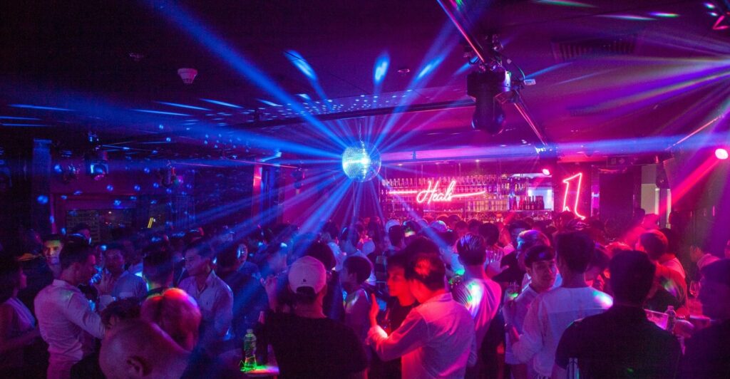 Crowd of enthusiastic guests at the House of Heals, immersed in the lively ambiance with colorful spotlights highlighting the venue's energetic and inclusive drag scene.
