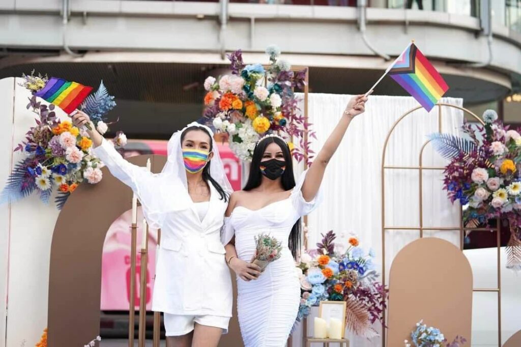 Two queer women waving rainbow flags at Pride event in Bangkok