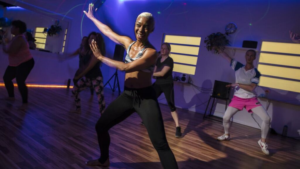 A vibrant scene of LGBTQIA+ women joyfully dancing together at Everybody Gym in Los Angeles, embodying the spirit of inclusive fitness. The gym, known for its focus on providing a safe and welcoming space for the LGBTQIA+ community in the U.S., is filled with diverse individuals celebrating their identity through movement and exercise.