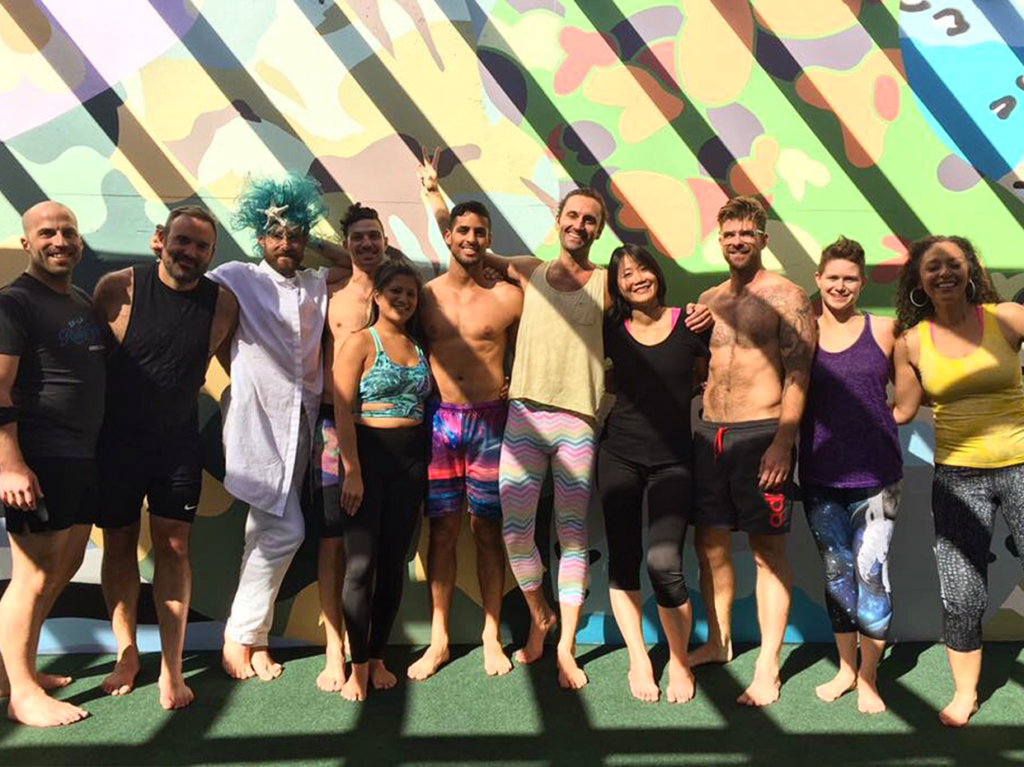 A diverse group of LGBTQIA+ individuals posing confidently in front of a vibrant, colorful wall at Everybody Los Angeles gym, symbolizing inclusive fitness and community in the U.S.