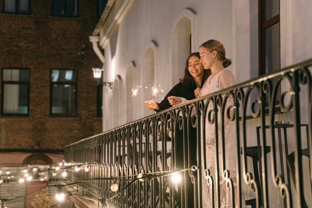 Image of two women in love, holding hands, and standing on a romantic balcony at night with twinkling lights, enjoying a beautiful Valentine's Day date in Los Angeles. This LGBT-friendly spot is perfect for celebrating love and creating unforgettable memories.