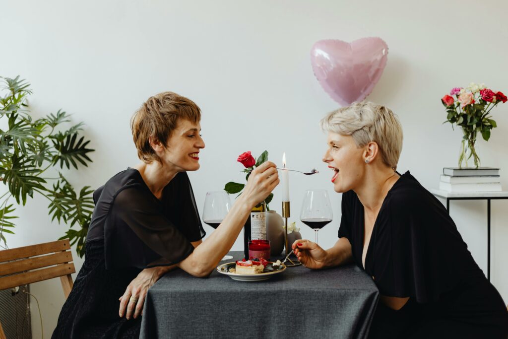 Lesbian couple enjoying Valentine's Day with a romantic dinner, one holding a spoon suggestively towards the other's lips in a playful gesture