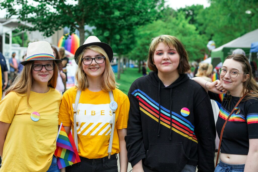 Four LGBTQIA+ women in rainbow shirts and hats