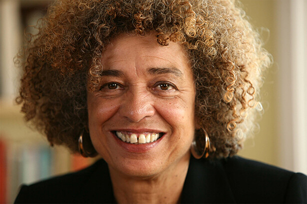 Photo of Angela Davis, a Black activist with an afro hairstyle, smiling warmly. She is wearing a black suit