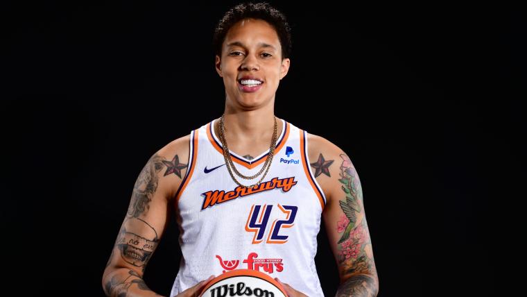Basketball player Brittney Griner in a basketball uniform, holding a basketball and smiling confidently.