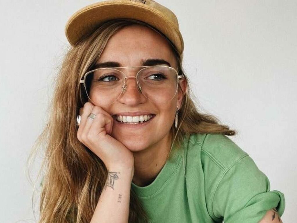 Australian musician G-Flip with a big smile, sporting glasses and a green top.