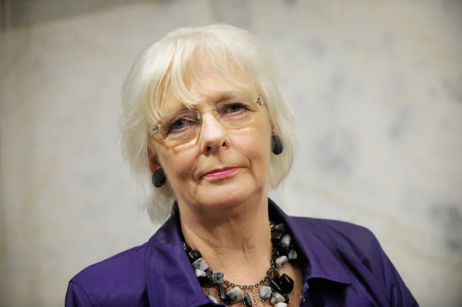 Portrait of Jóhanna Sigurðardóttir, a woman with short white hair and wearing a purple shirt, looking directly at the camera.