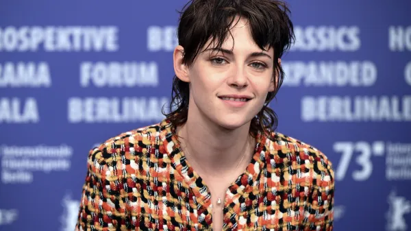 Close-up photo of actress Kristen Stewart smiling brightly. She has short, black hair and is wearing a colorful shirt.