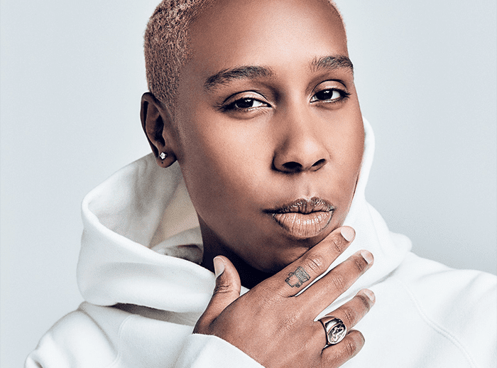 Close-up portrait of Lena Waithe, a Black woman with short hair, wearing a white hoodie and looking confidently at the camera.