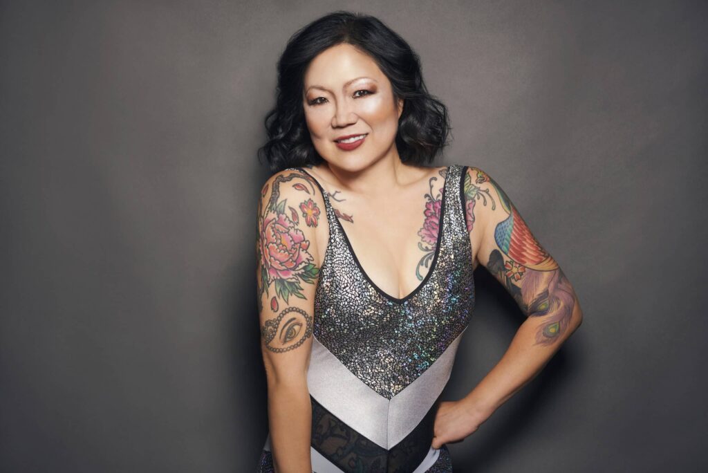 Comedian Margaret Cho strikes a confident pose, showcasing her tattooed arms.