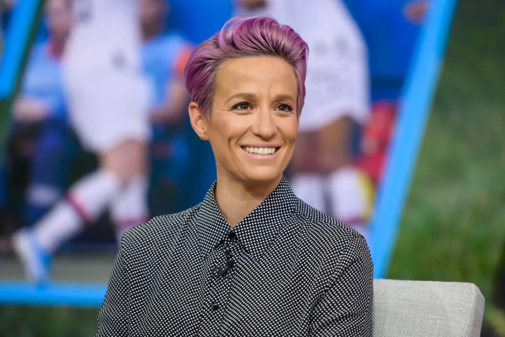 Photo of Megan Rapinoe, a professional soccer player, with short pink hair. She is smiling confidently and posing.