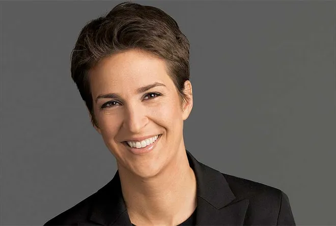 Photo of Rachel Maddow, a television host, confidently posing with a smile. She is wearing a black t-shirt.