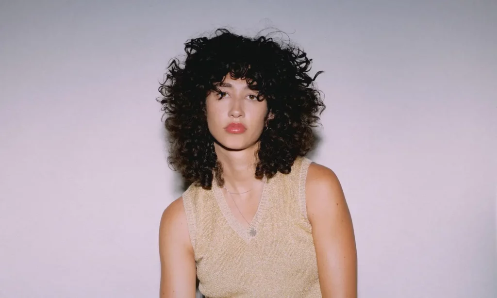 Photo of Towa Bird, a singer, with afro hairstyle. They are posing confidently against a white background.