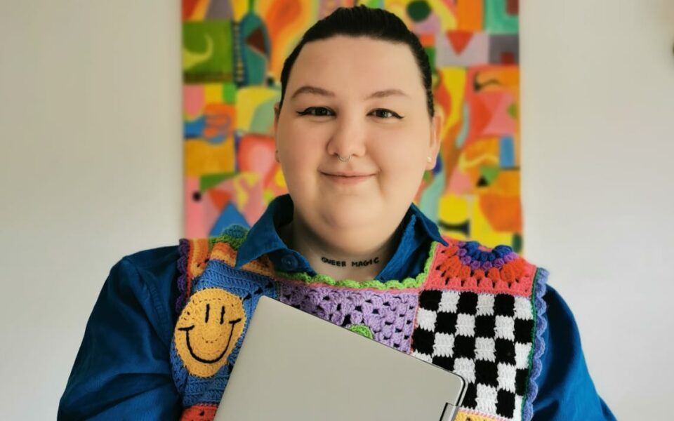 Wednesday Holmes smiling and wearing colourful costumes with a colourful background