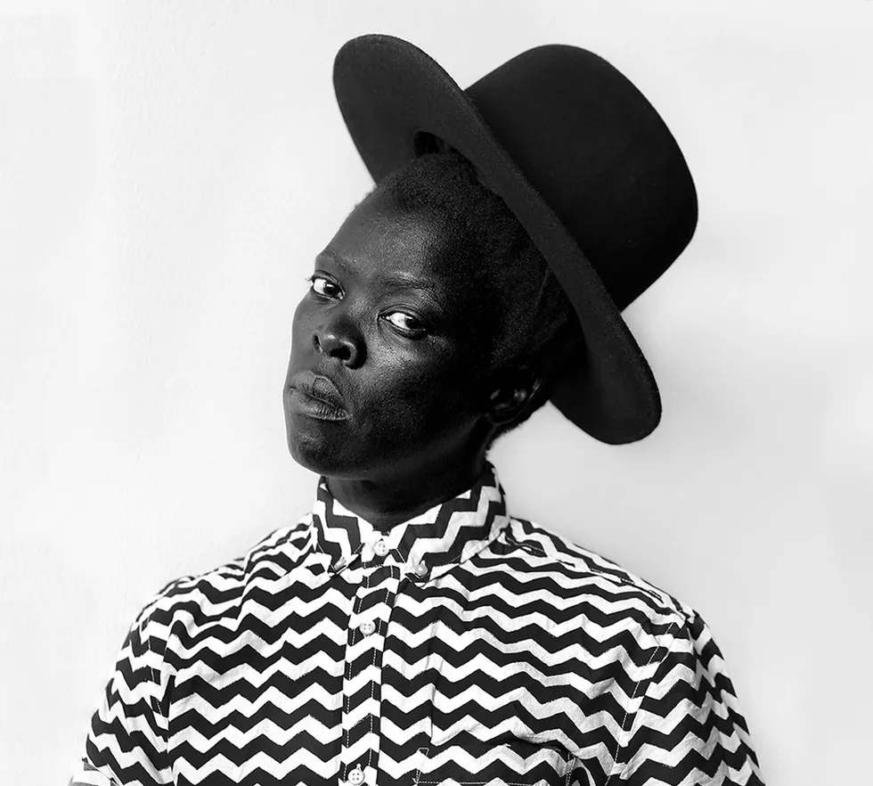 Black and white portrait of Zanele Muholi, a South African visual activist, gazing confidently at the viewer.