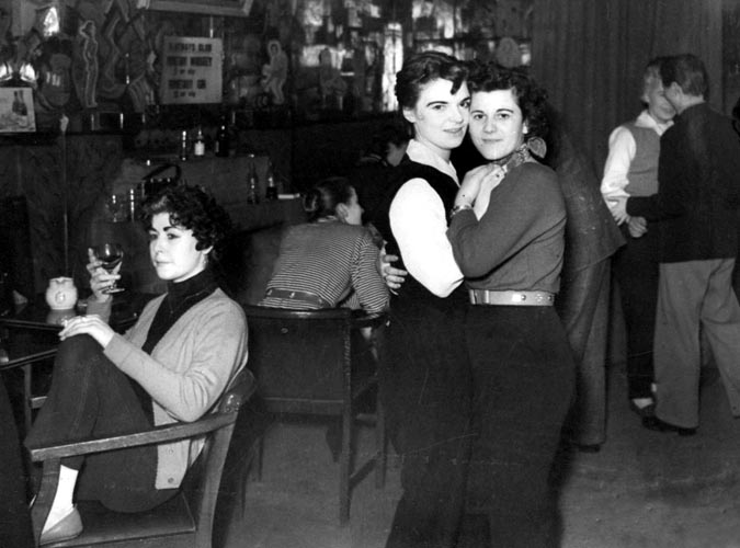 Two women embracing and dancing joyfully, gazing at the camera and other lesbians enjoying their time in 1931 inside Gateways Club, the UK's First Lesbian Bar/Club